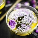 A glass teacup filled with tea from roses, topped with purple flower petals and a small purple rose bud.