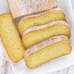 A sliced loaf of vanilla cake dusted with powdered sugar.