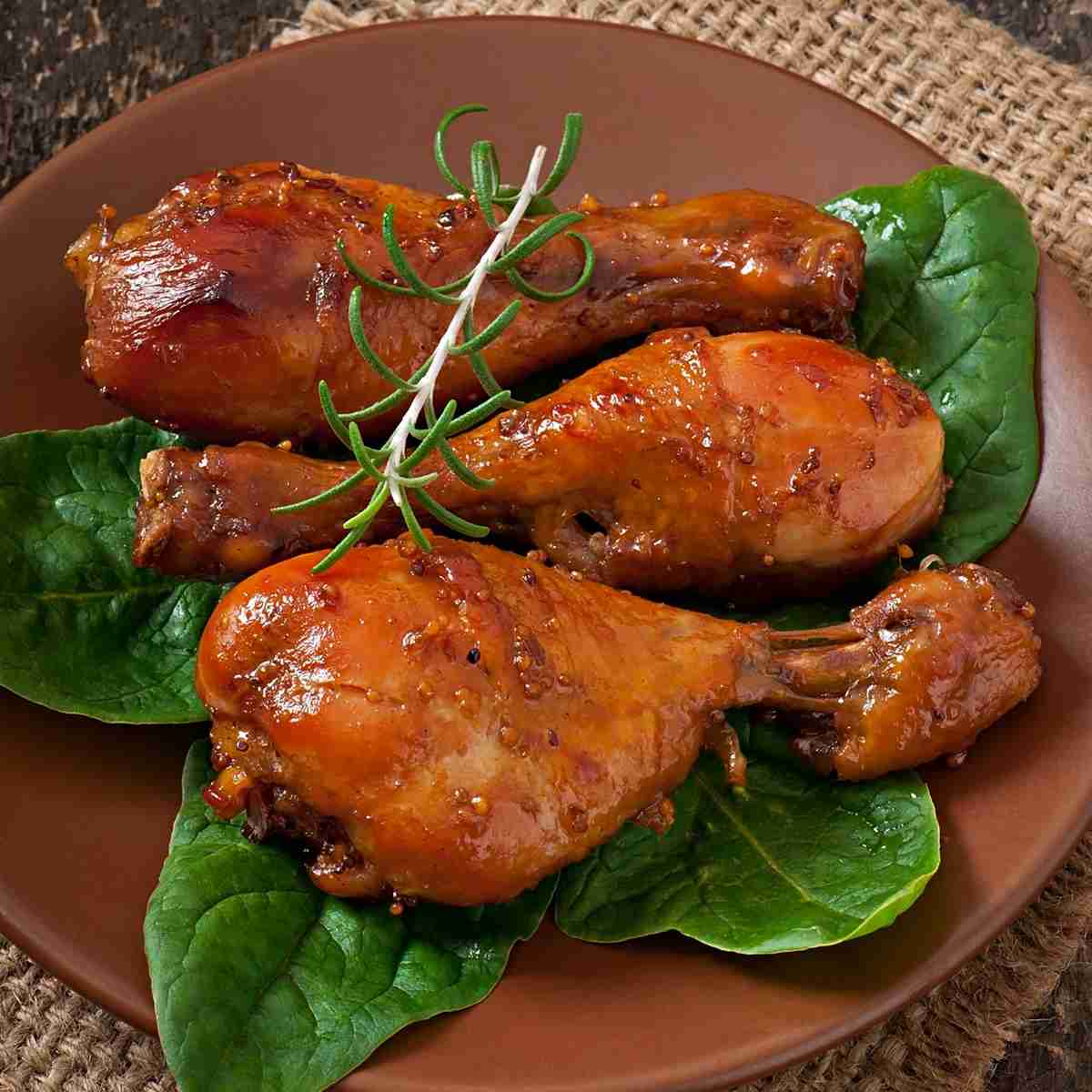 Three glazed chicken drumsticks garnished with rosemary.