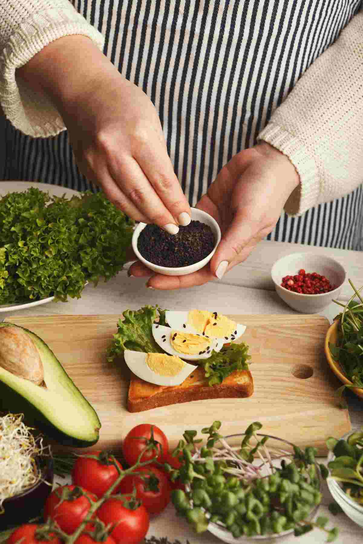 Adding seeds to a plate with sliced boiled egg and greens on toast.