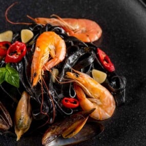 A plate of black pasta with shrimp, mussels, and sliced red chili.