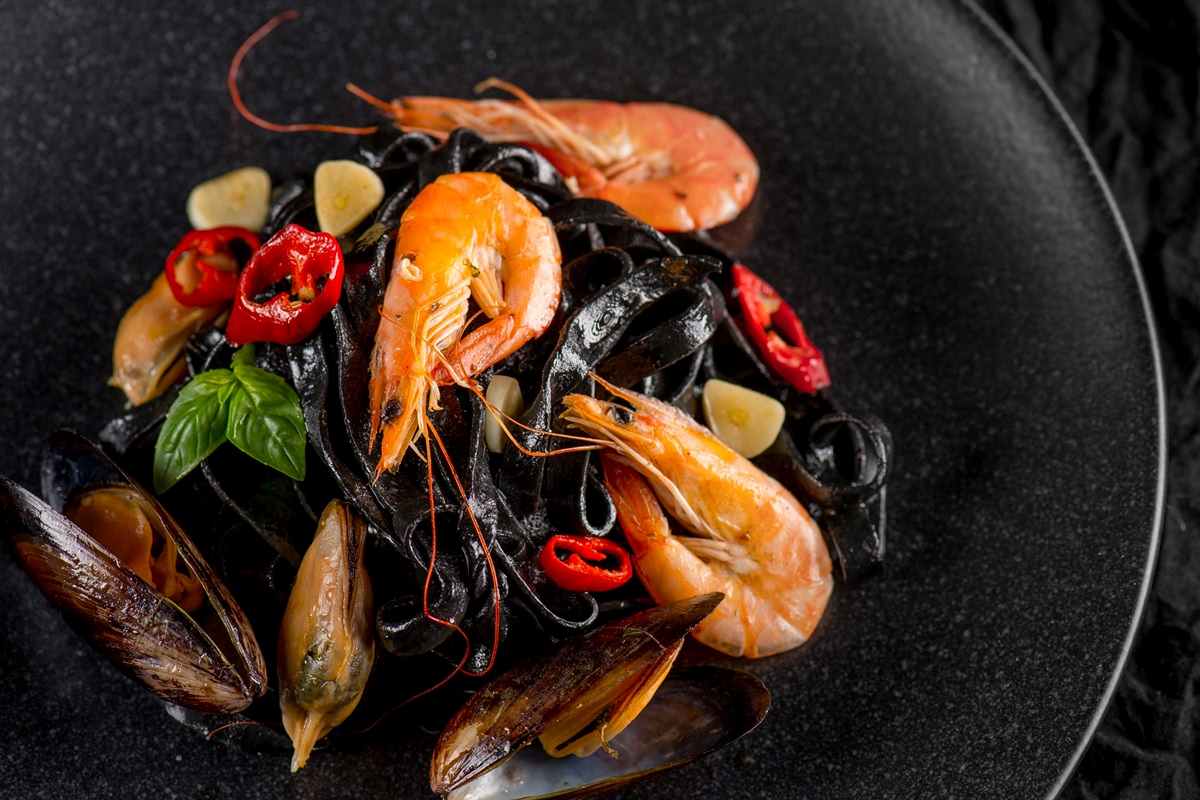 A plate of black pasta with shrimp, mussels, and sliced red chili.