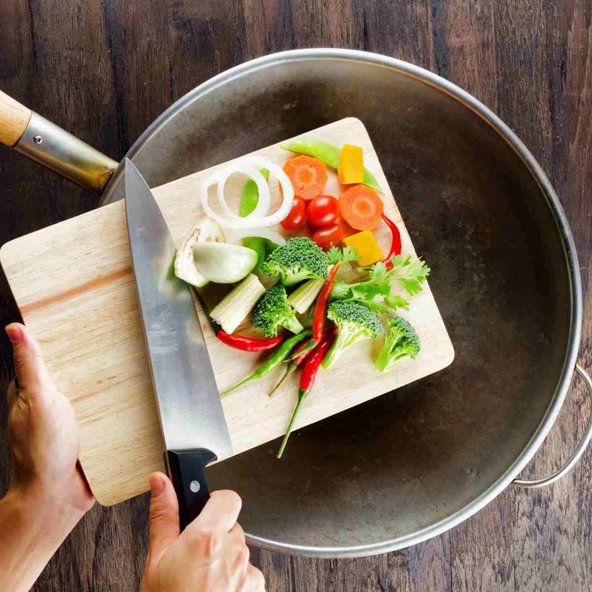 Hands holding a wooden cutting board with chopped vegetables.