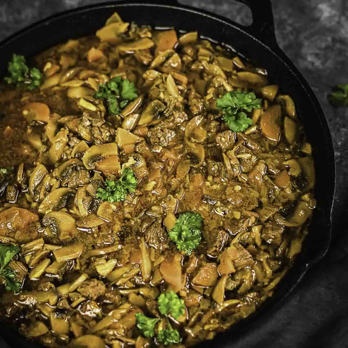A cast iron pan filled with a mushroom stew, garnished with parsley.