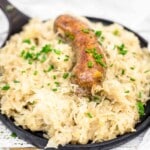 A cooked sausage on a bed of sauerkraut, garnished with chopped chives, served in a black skillet.