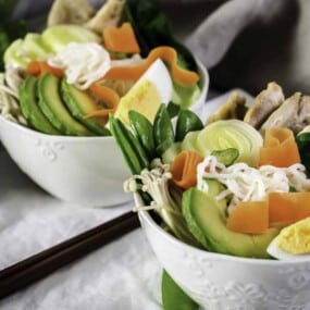 Two bowls of spicy ramen noodles with veggies on top.