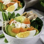 Bowl of ramen with noodles, avocado, boiled egg, spinach, carrots, mushrooms, and chicken.