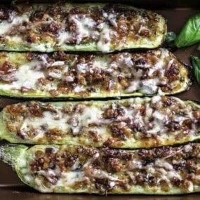 A baking tray with stuffed zucchini boats topped with cheese.