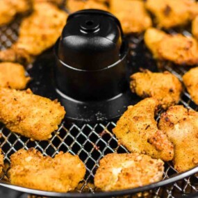 Breaded chicken pieces cooking in an air fryer basket.