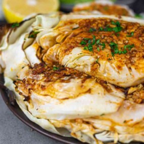Grilled cabbage topped with chopped herbs and spices on a dark plate.