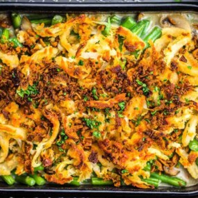 A baked green bean casserole topped with crispy fried onions in a black rectangular dish, with visible green beans and mushrooms underneath.