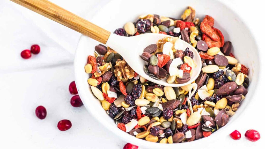 A bowl of mixed nuts, seeds, dried fruit, and chocolate chips with a wooden spoon.