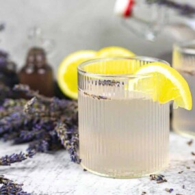 Two glasses of lavender lemonade with lemon slices on the rim, surrounded by fresh lavender sprigs.