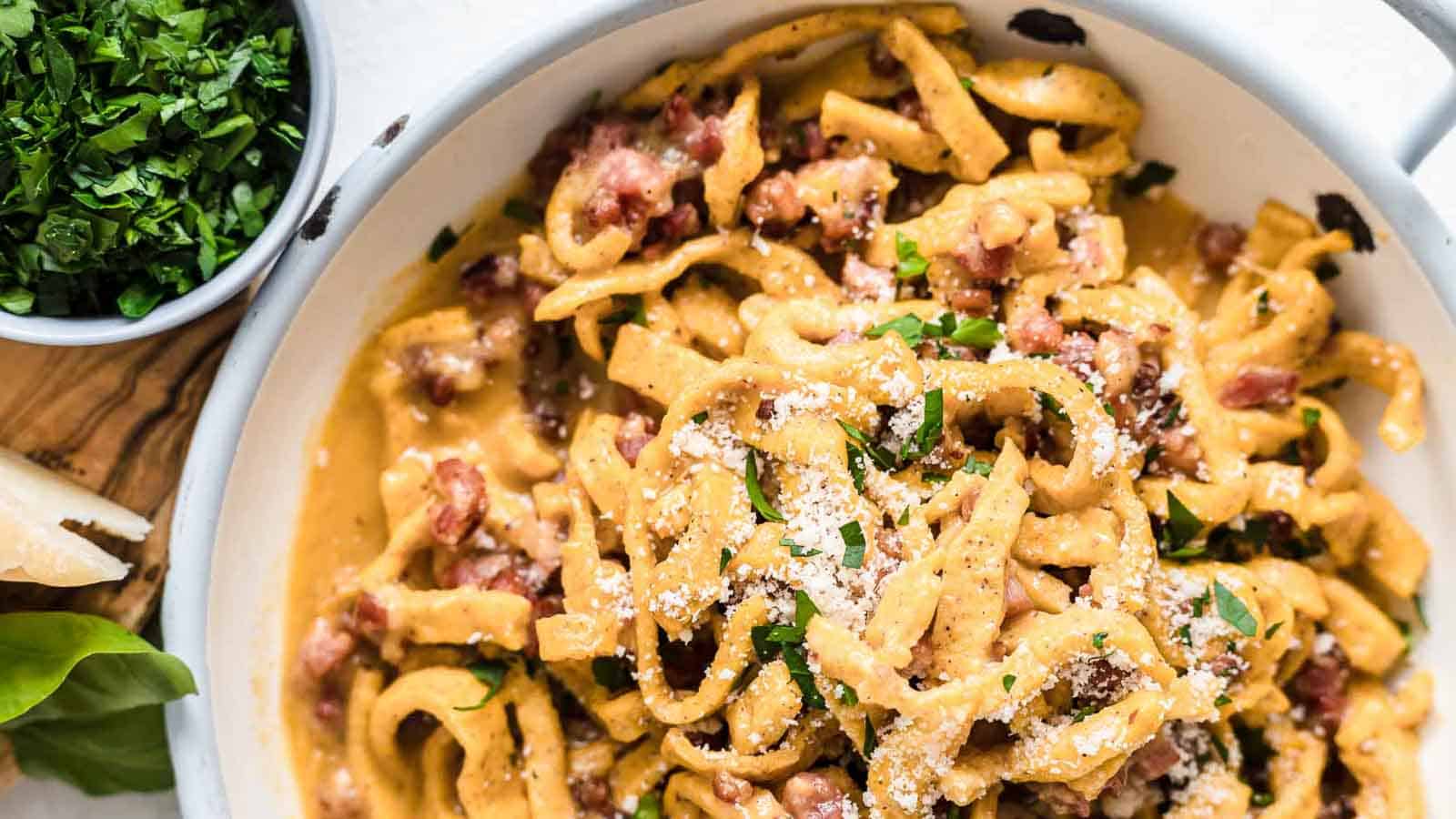 A plate of pasta carbonara topped with grated cheese and chopped parsley, complemented by a bowl of fresh herbs on the side to stay balanced and delightful.