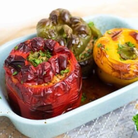 Three stuffed bell peppers in a baking dish; one red, one green, and one yellow. Garnished with herbs.