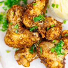 Fried chicken pieces garnished with chopped herbs, served on a plate next to a small cup of butter.