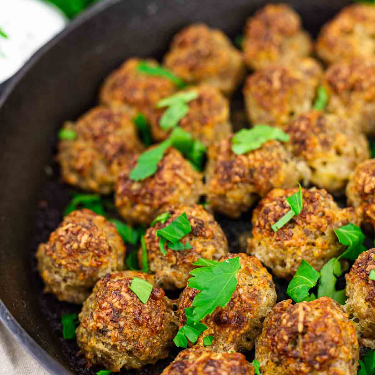 A cast iron skillet filled with browned meatballs garnished with chopped fresh parsley.