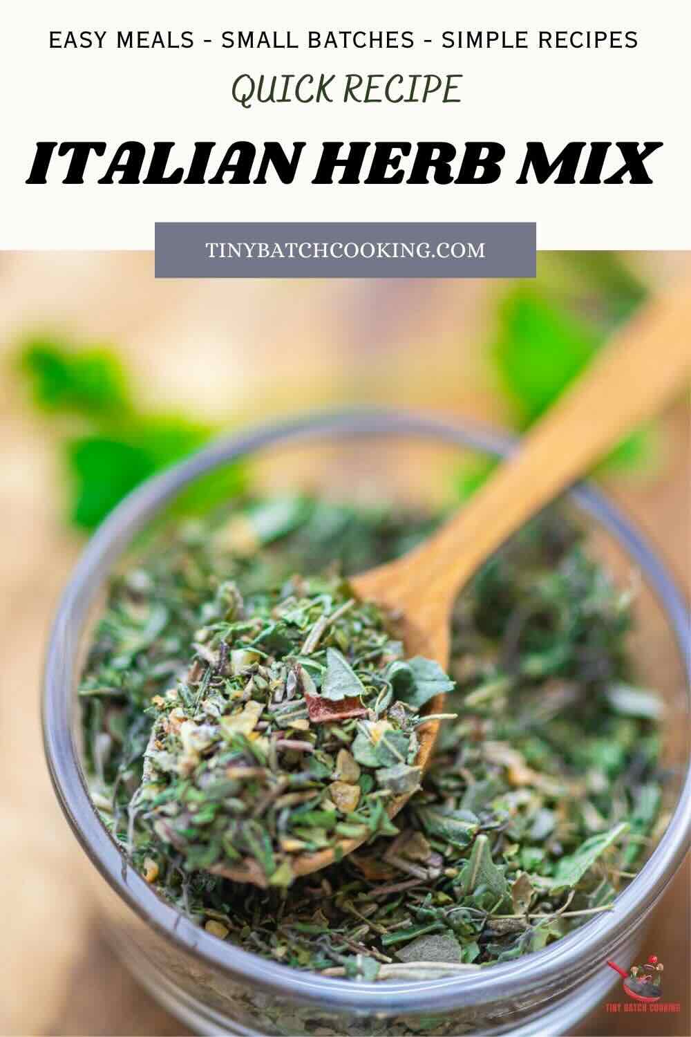 A glass jar filled with Italian herb mix sits on a table, with a wooden spoon scooping some of the herb blend.