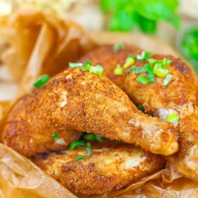 Two pieces of seasoned, crispy fried chicken garnished with chopped green onions on brown parchment paper.