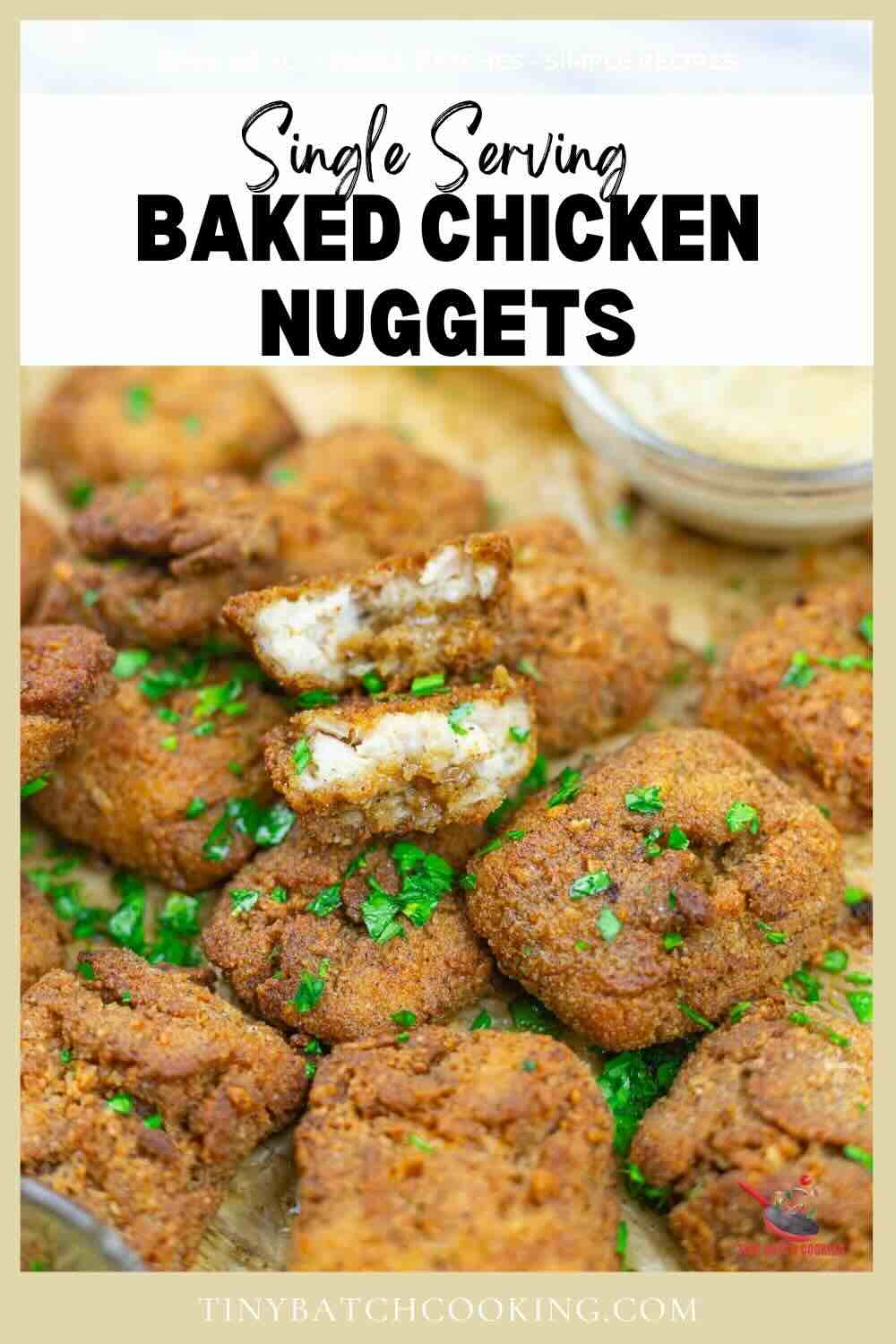 A close-up of several baked chicken nuggets garnished with chopped parsley, with one nugget broken open to show the inside. A small container of dipping sauce is in the background.