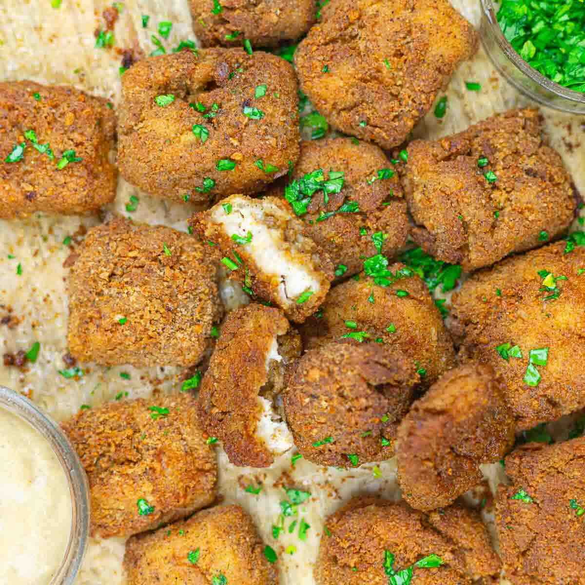 Breaded and fried tofu cubes garnished with chopped herbs, served with dipping sauces on the side.
