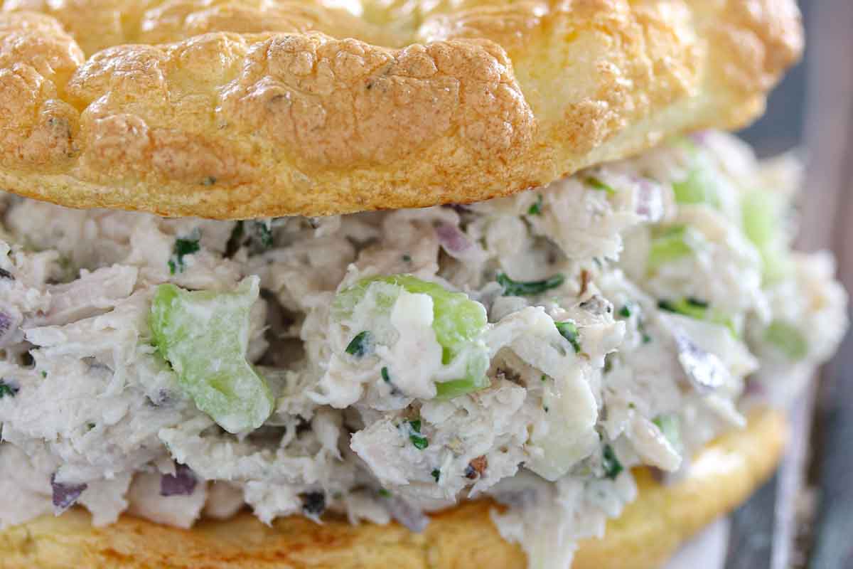 Close-up of a chicken salad sandwich with visible chunks of chicken, celery, and herbs, served in a fluffy, golden bread roll.