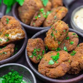 Several bowls filled with golden-brown falafel patties garnished with chopped herbs, accompanied by a small bowl of creamy dipping sauce.