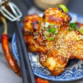 Grilled chicken wings topped with sesame seeds and chopped green onions, served on a blue patterned plate with chopsticks.