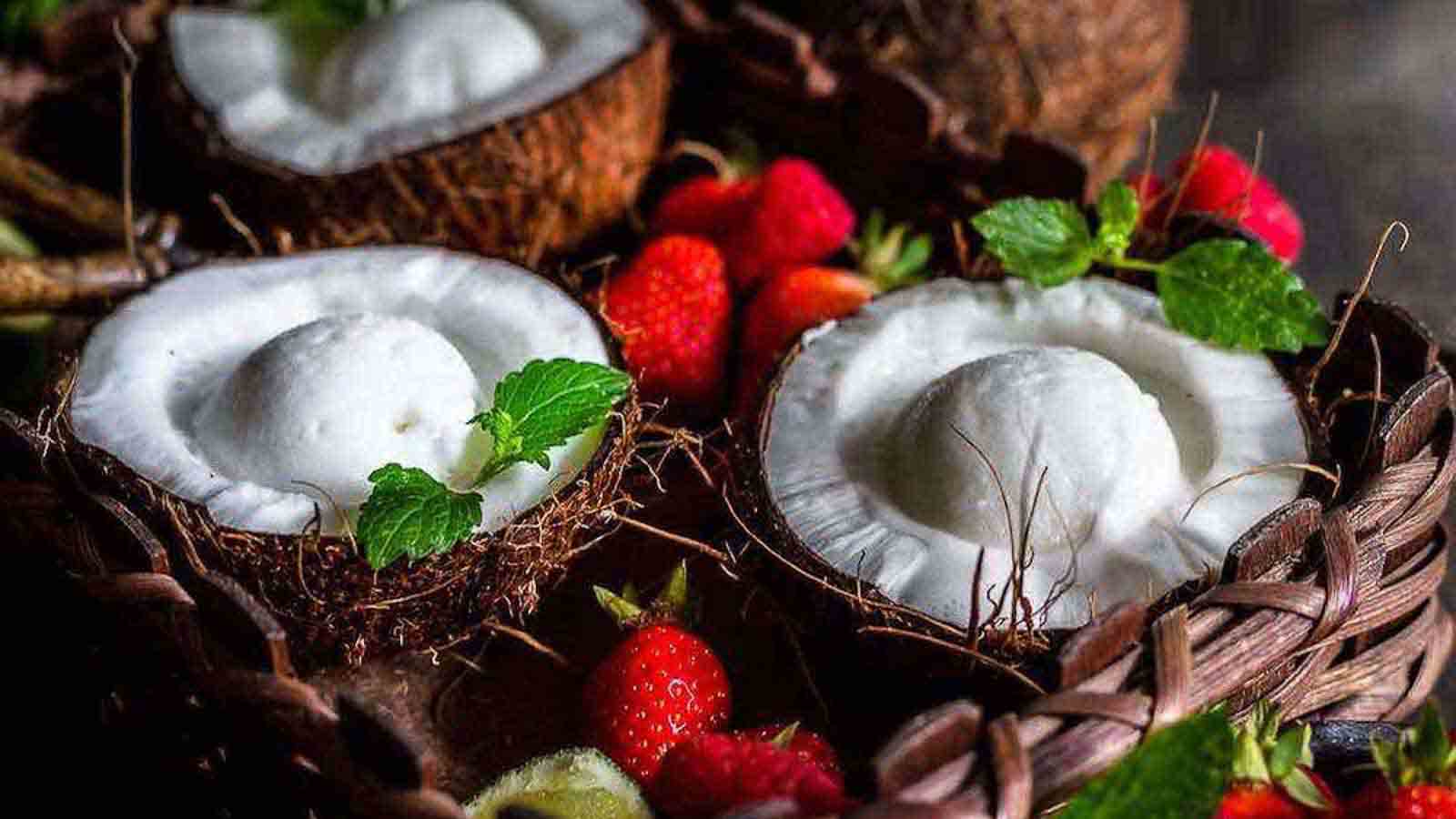 Halved coconuts filled with coconut ice cream are arranged in a basket with strawberries, mint leaves, and lime slices—one of the easy desserts that ensures summer ends better.