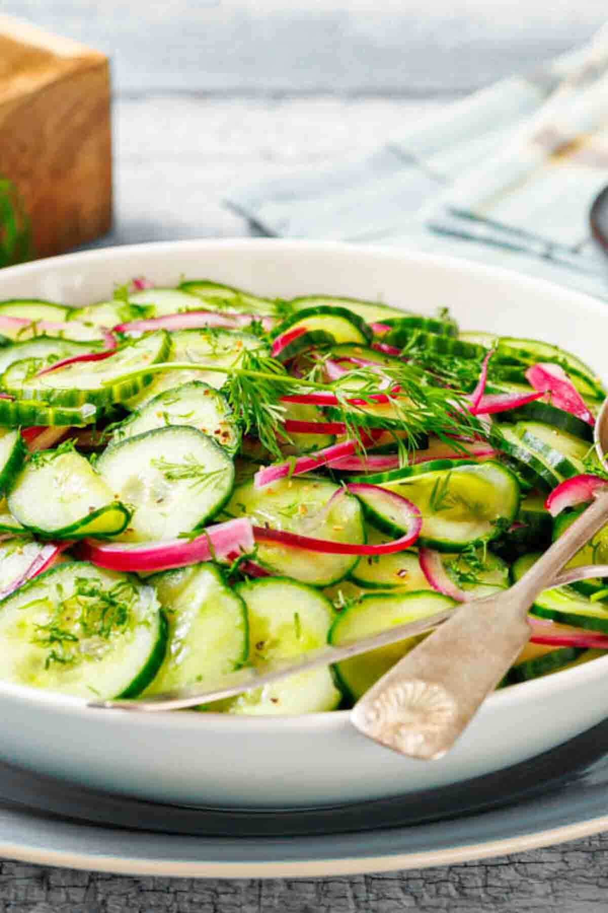 A bowl of cucumber salad with sliced cucumbers, red onions, and fresh dill, served with a spoon.