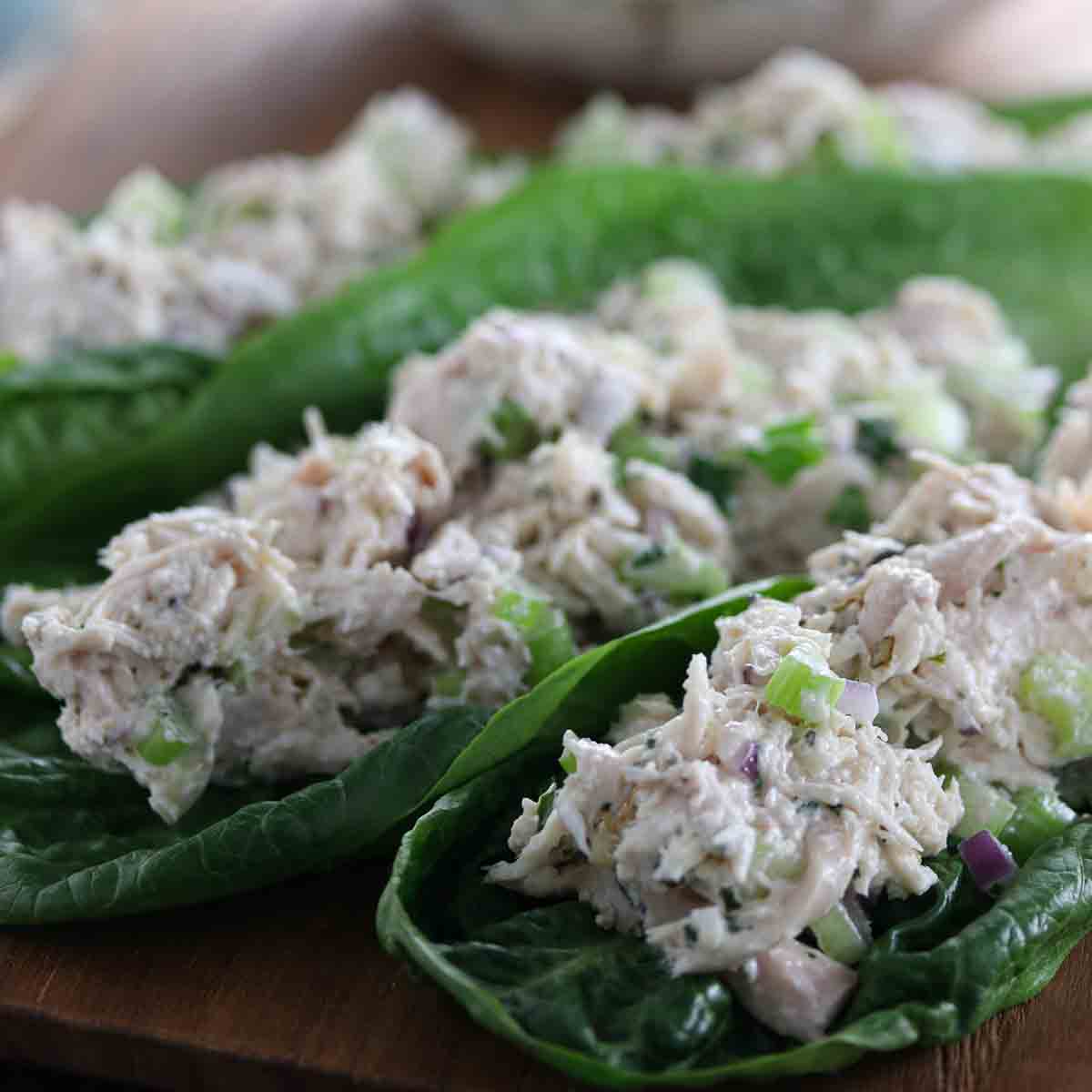 Chicken salad with chopped vegetables served on romaine lettuce leaves, arranged on a wooden surface.