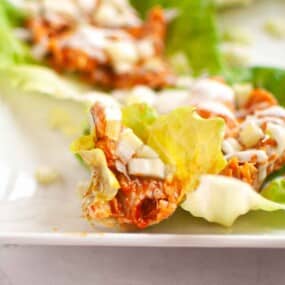 A close-up of lettuce wraps filled with shredded meat, diced onions, and melted cheese on a white plate.