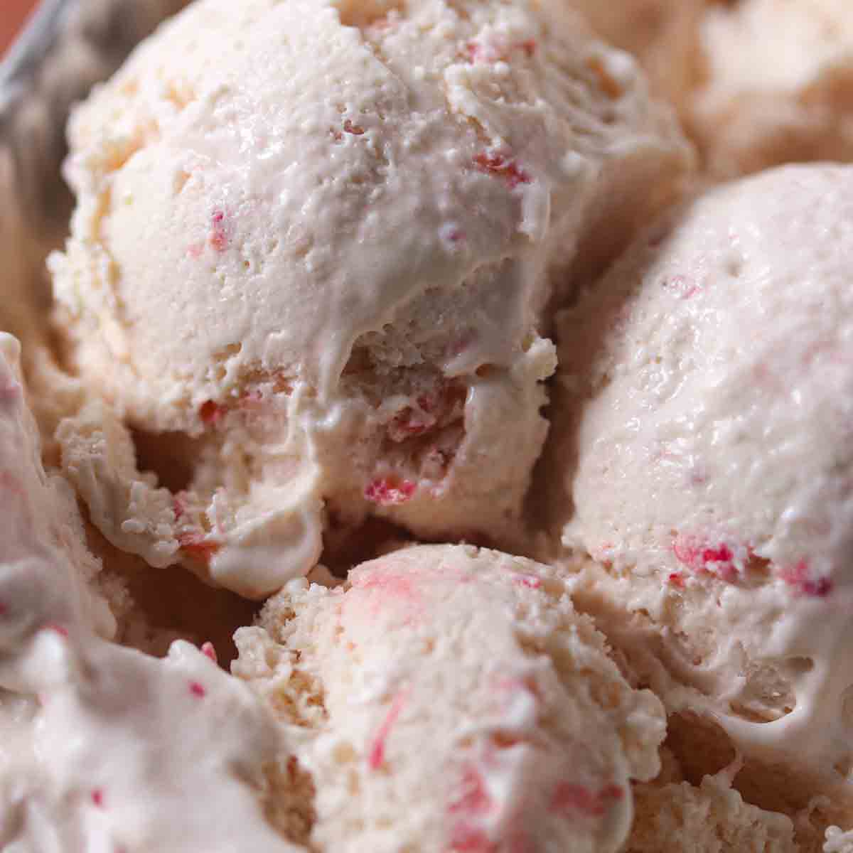 Close-up of several scoops of vanilla ice cream with small pink streaks throughout.
