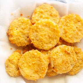 A plate lined with paper towels holds several golden brown, breaded and fried round slices of food, likely fried green tomatoes.