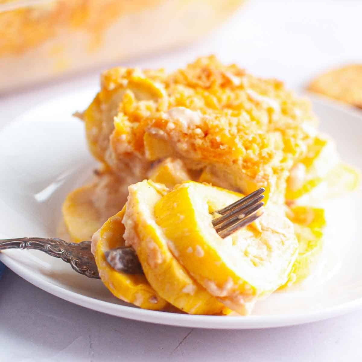 A white plate with a serving of yellow squash casserole topped with a breadcrumb crust, with a fork resting on the side.