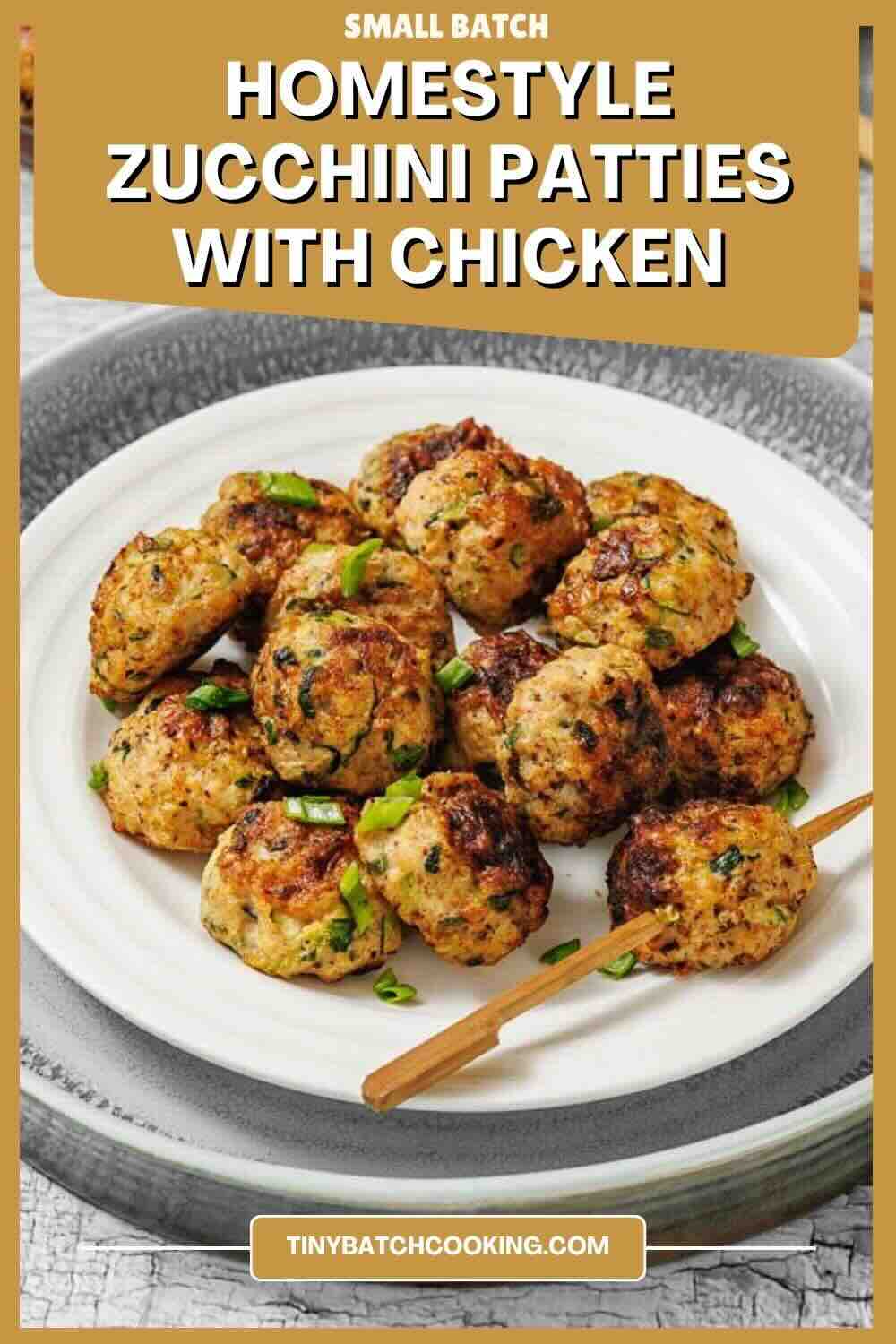 A white plate with several browned zucchini and chicken patties garnished with green herbs, placed on a gray surface.