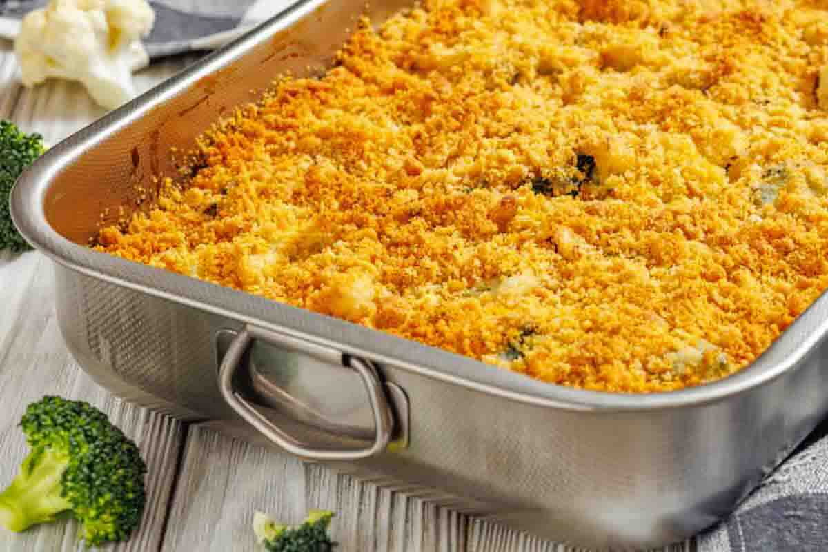 A metal baking dish filled with baked casserole topped with a golden, crispy breadcrumb layer, with broccoli florets visible on the table nearby.