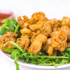 A plate of fried chicken pieces served on a bed of fresh arugula, with a small bowl of dipping sauce in the background.
