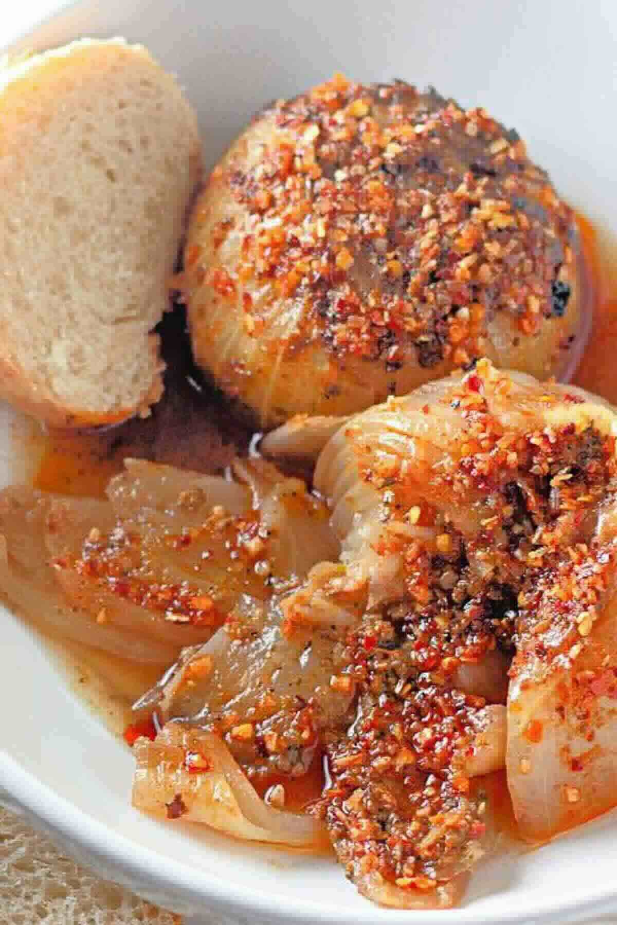 A plate with a seasoned roasted onion, slices of cooked onion in sauce, and a piece of bread.