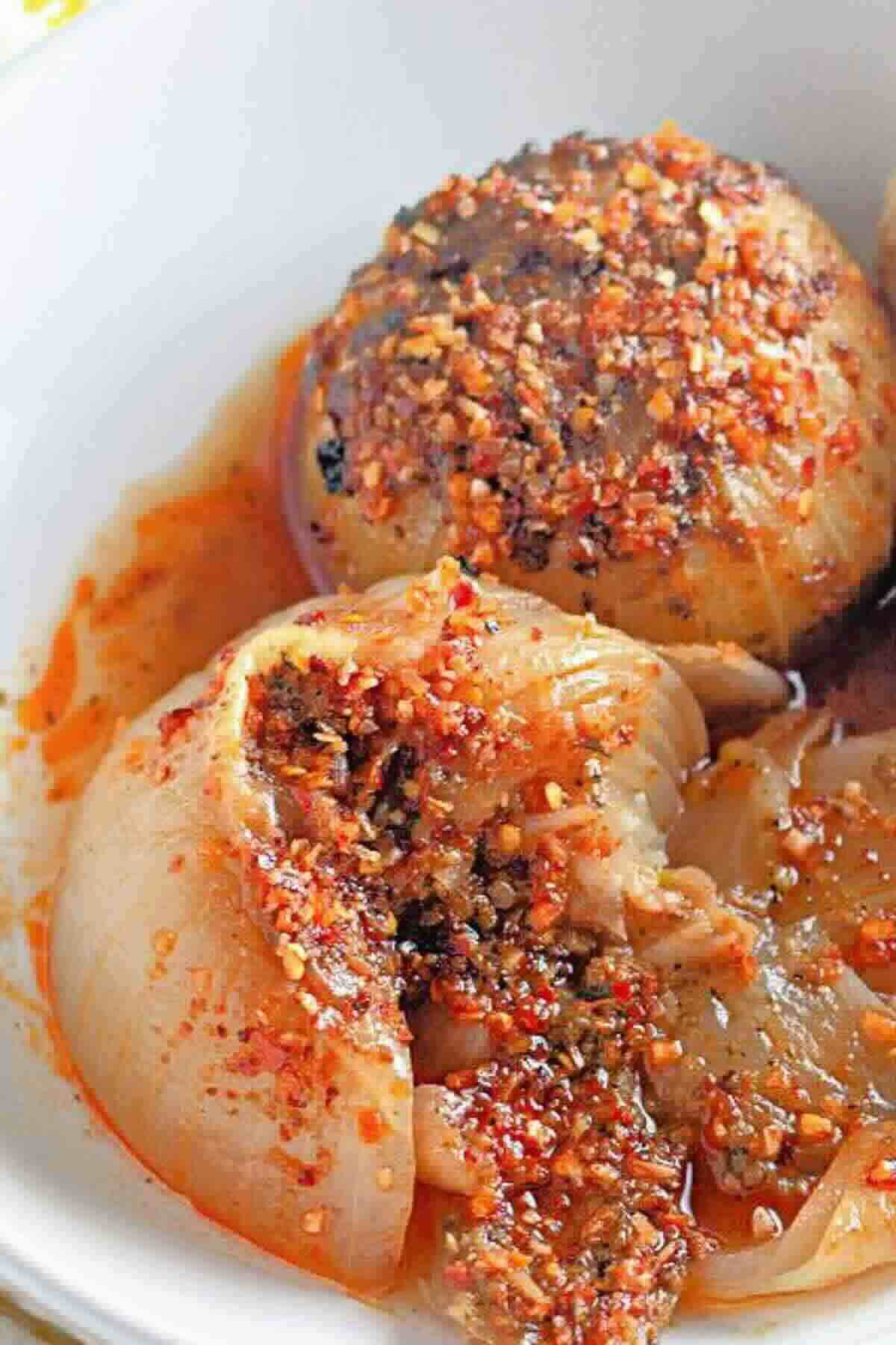 Whole onions stuffed with minced meat and spices, baked and topped with a red, oily seasoning blend, served in a white dish.