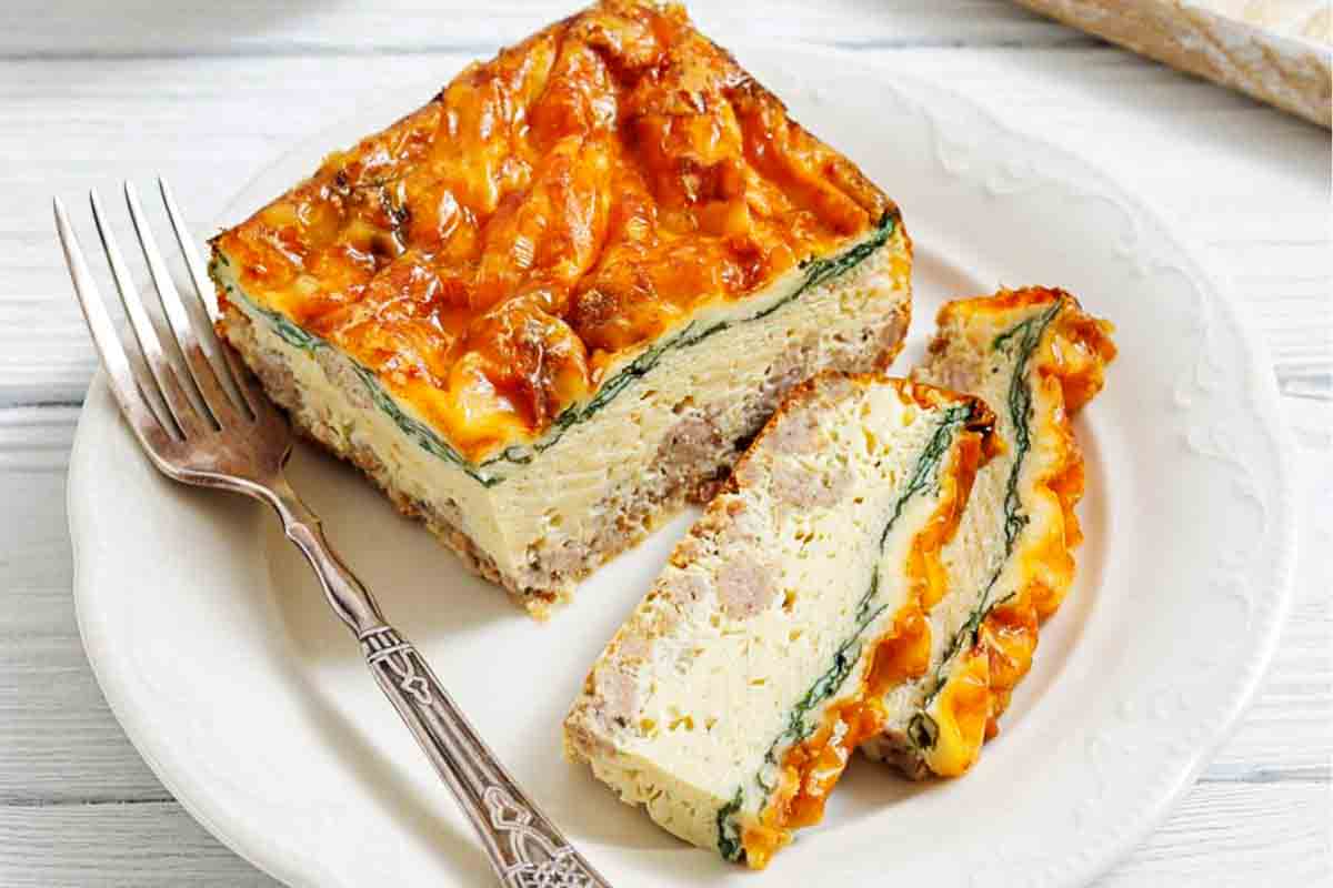 A plate with a large rectangular slice and a smaller slice of baked egg casserole containing ground meat, spinach, and melted cheese, with a fork beside them.