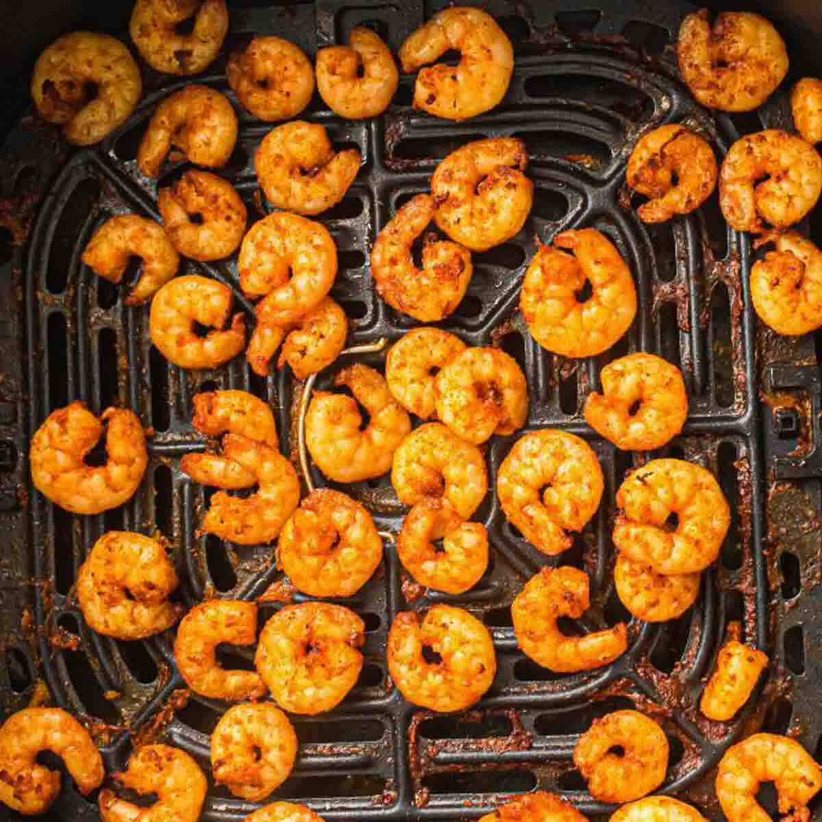 Cooked, seasoned shrimp arranged in a single layer on the basket of an air fryer.