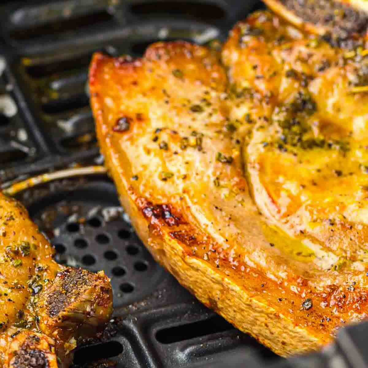 Two seasoned pork chops are cooking on a black air fryer tray, showing a golden-brown, slightly crispy exterior.