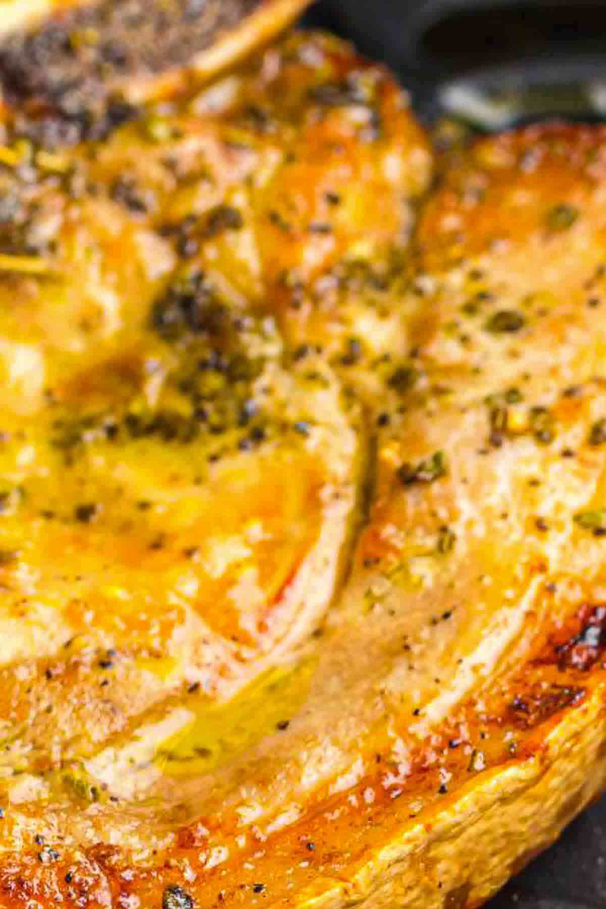 Close-up of a cooked, seasoned pork chop with a golden-brown crust and visible herbs.
