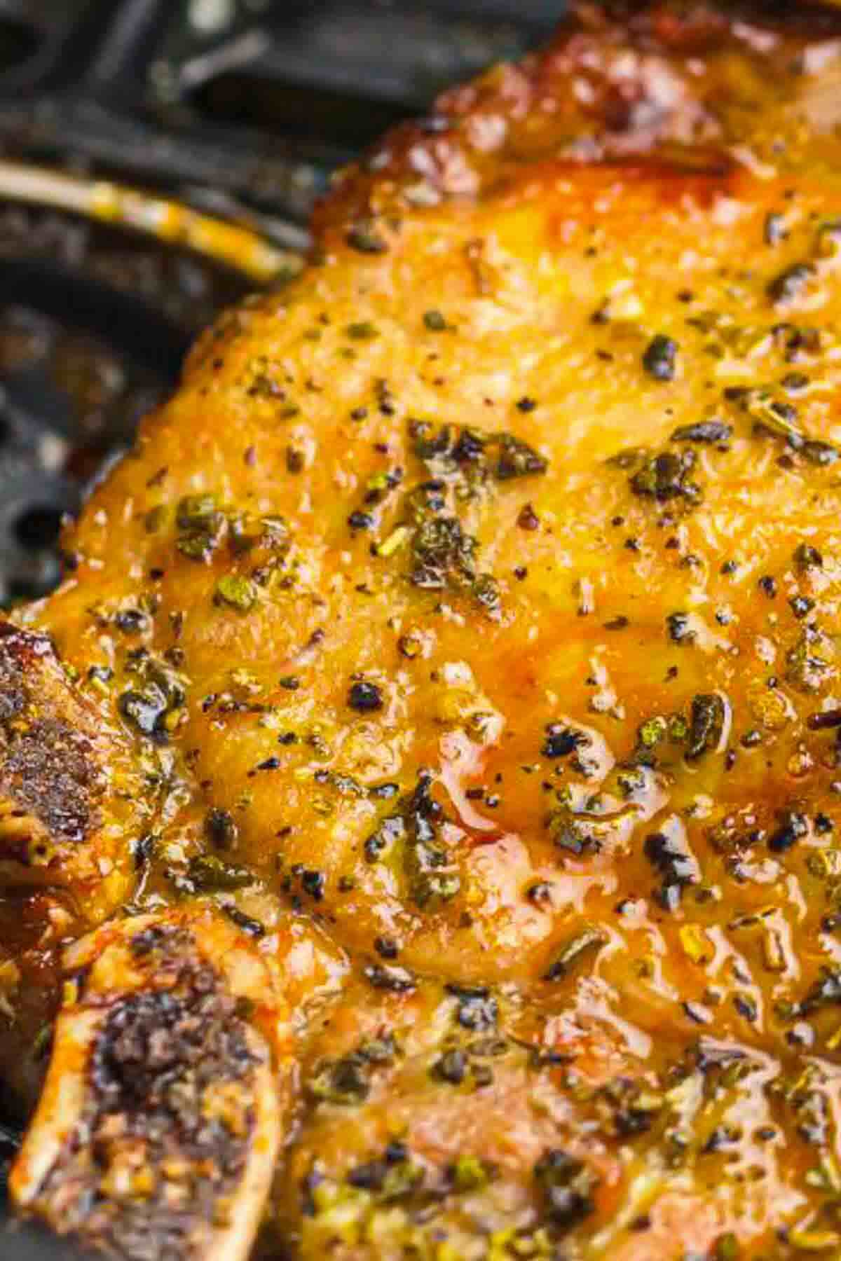 Close-up of a cooked, seasoned pork chop with visible herbs and juices on the surface.