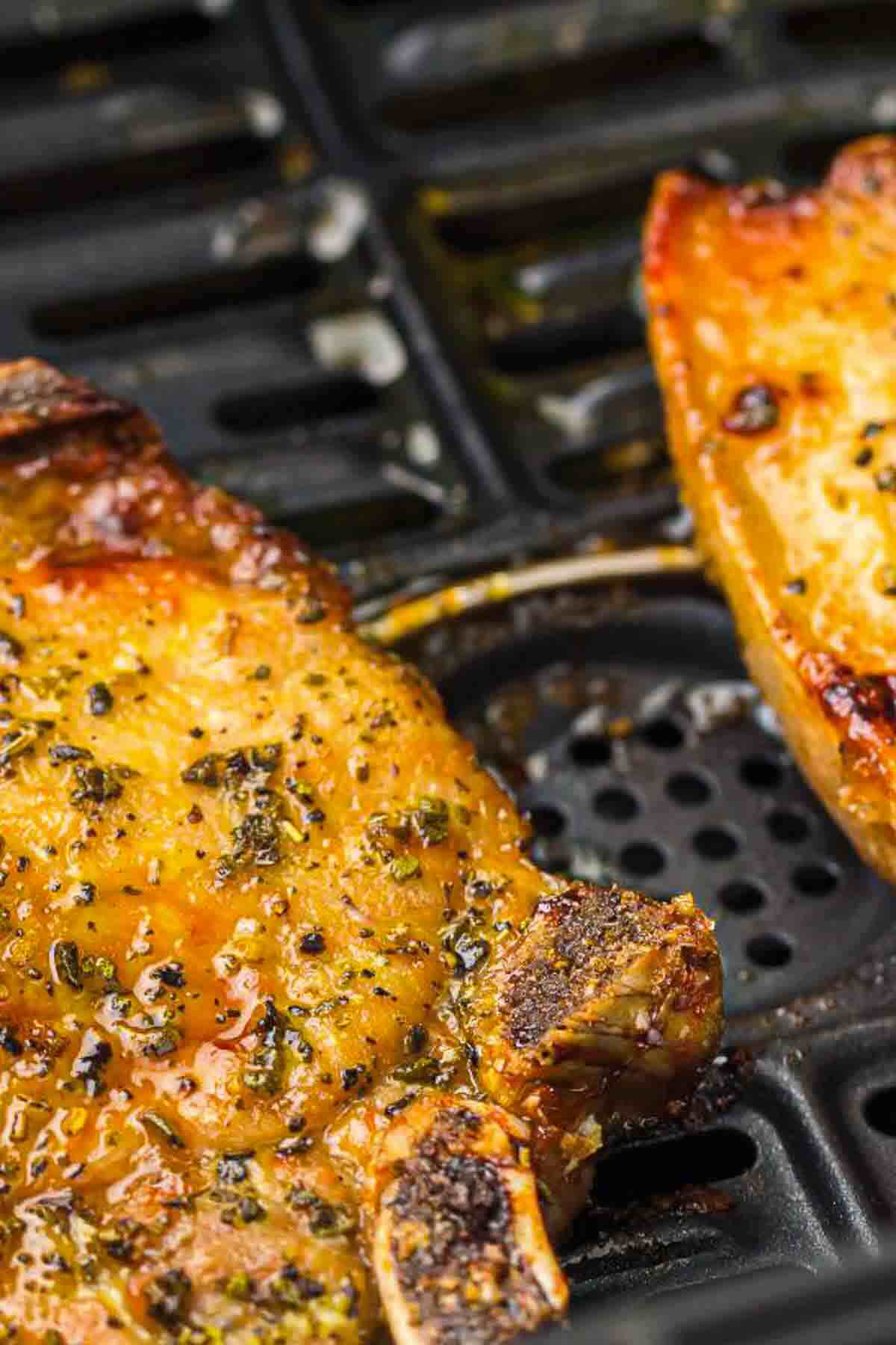 Close-up of seasoned pork chops cooking on a grill, showing grill marks and a glazed surface.