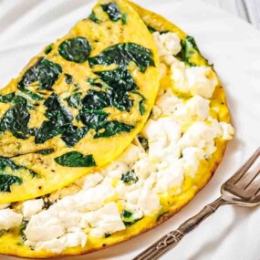 A spinach and feta cheese omelette is folded on a white plate with a fork beside it.