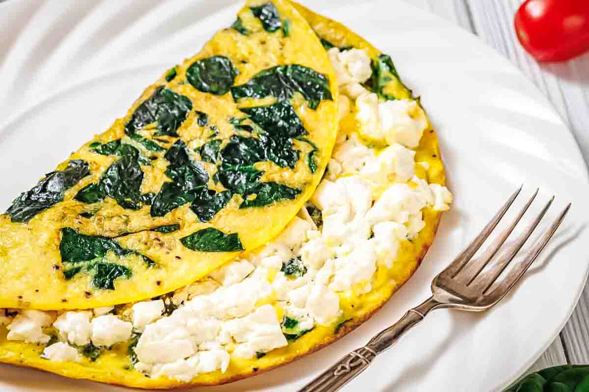 A spinach and feta cheese omelette is folded on a white plate with a fork beside it.