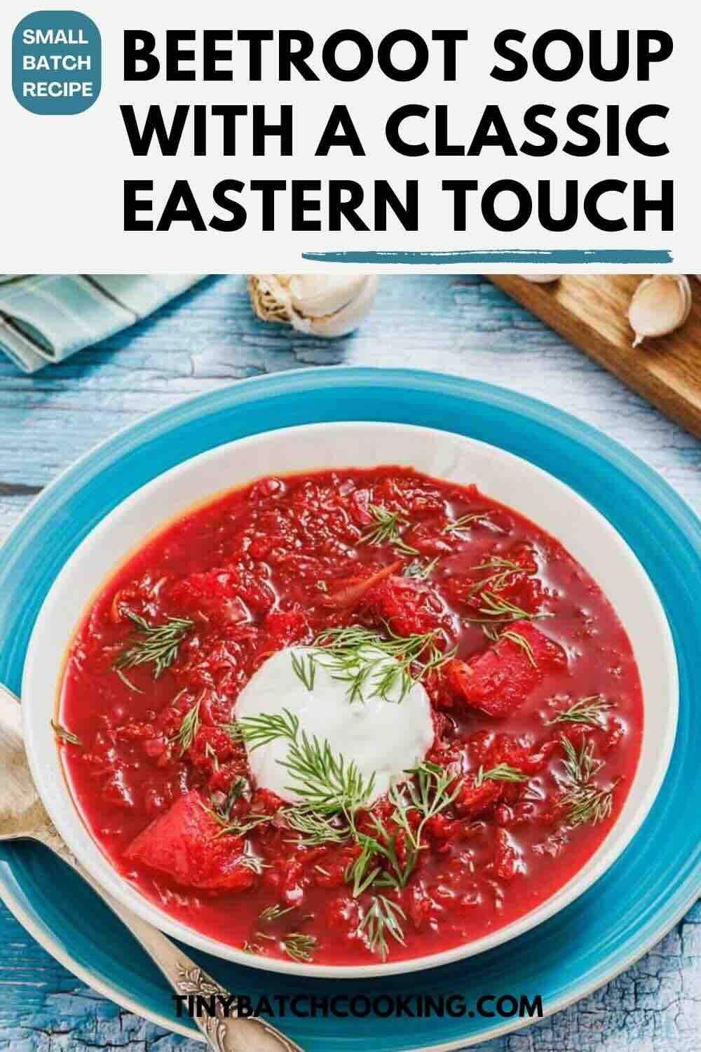 A bowl of beetroot soup garnished with a dollop of sour cream and fresh dill, placed on a blue plate with a spoon on the side.