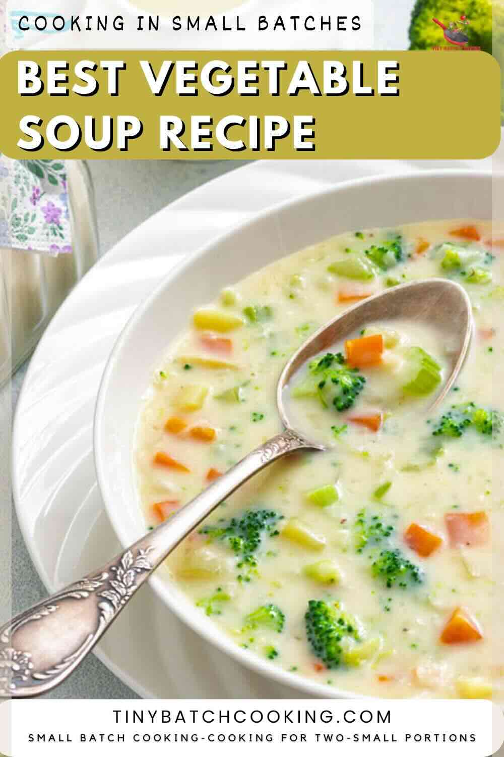 A bowl of creamy vegetable soup with broccoli, carrots, and celery on a white plate, with a silver spoon resting inside the bowl.